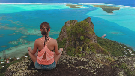 Young woman is practicing yoga and enjoying a moment of peace while admiring the scenic view of maupiti island lagoon in french polynesiaの写真素材