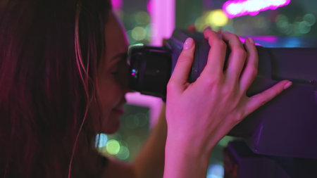Woman on a rooftop at night, using binoculars to observe the vibrant city lights below, filled with wonder and excitementの写真素材