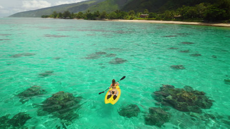 Aerial view of a young woman enjoying paddleboarding in a stunning tropical lagoon with turquoise...