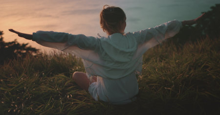 Young woman meditates and practices yoga on a hill at sunset, feeling free and connected to nature