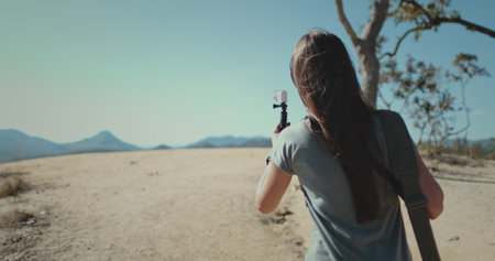 Travel blogger woman shooting on camera beautiful mountain landscape. Girl walk hold record on gopro, back view. Outdoor lifestyle travel on summer holiday vacation. Pai Canyon Chiang Mai , Thailand.の写真素材
