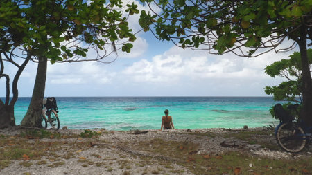 Relaxing at a tropical beach, a woman enjoys the stunning view of a turquoise lagoon on a sunny day, surrounded by natures beautyの写真素材