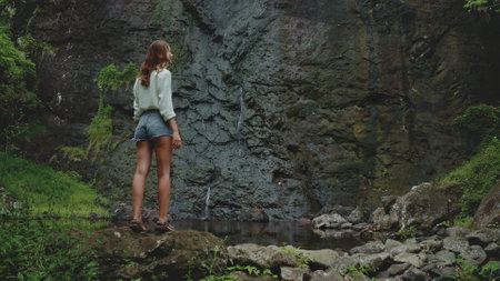 Woman enjoying a waterfall view in nature, perfect for adventure seekers. A serene setting for exploration in the outdoorsの写真素材