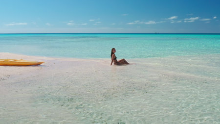 Woman is enjoying the tranquility of a secluded beach, with crystal-clear turquoise water gently lapping at the shore and a kayak resting on the pristine sandの写真素材
