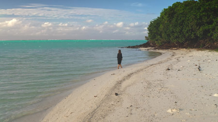 Woman is enjoying a peaceful stroll along a secluded beach, taking in the breathtaking beauty of the turquoise lagoon and lush green vegetationの写真素材