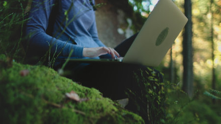 Woman peacefully works on her laptop outdoors in the lush carpathian mountains, finding inspiration and tranquility in the serene settingの写真素材