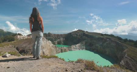 A woman is standing on top of a mountain overlooking a lake. The scenic view shows the beauty of the surrounding landscape, including a volcano and crater lake in the Philippines.の写真素材