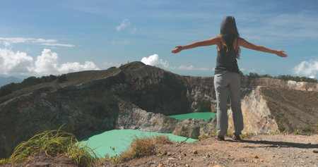 Woman raise hands on volcano mountain crater edge. Volcanic blue crater lakes. Travel destination. Beautiful wild landscape. Female tourist on summer vacation. Lifestyle holiday conceptの写真素材