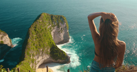 Young tourist woman is touching her hair while enjoying the view from a cliff on kelingking secret point beach in nusa penida, baliの写真素材