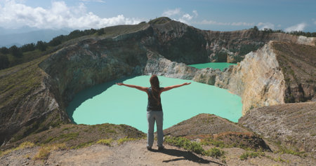 Young woman is embracing the breathtaking beauty of the turquoise crater lake of a volcano, feeling a sense of awe and wonder amidst the stunning natural landscapeの写真素材