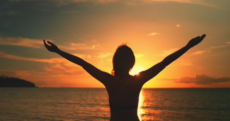 Woman hands up enjoy bright ocean sunset. Female silhouette against colorful sky, sun goes down in sea horizon. Lifestyle travel on summer holiday vacation, freedom, inspire. Back viewの写真素材