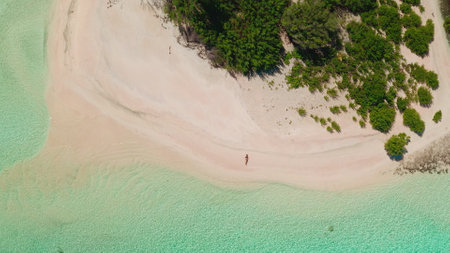 Woman enjoying a tranquil pink sand beach on a secluded tropical island in the maldives, with crystal-clear turquoise waters lapping at the shoreの写真素材