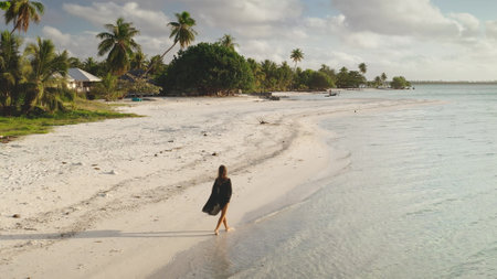 Young woman is enjoying a peaceful walk on a pristine beach in maupiti, french polynesia, as the sun sets over the horizonの写真素材