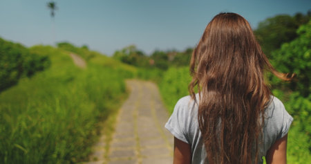 Long hair woman walking Campuhan Ridge Walk - tourist place to visit in Ubud, Bali island. Green field, blue sky. Outdoor lifestyle travel on summer holiday vacation. Close up back view,の写真素材