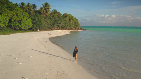 Young woman is walking on a pristine white sand beach of a tropical island, enjoying the turquoise lagoon and the lush green vegetationの写真素材