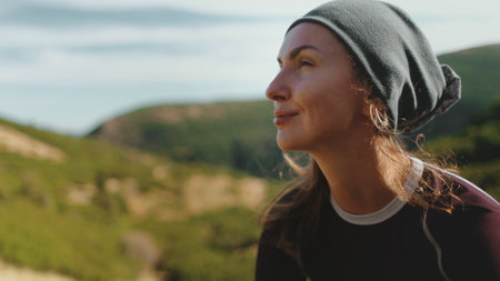 Trekking woman enjoy sunny day in Carpathian mountains. Caucasian girl in hat close up portrait looking on green hills and blue sky. Female tourist on summer vacation. Lifestyle holiday conceptの写真素材