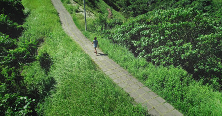 Aerial drone footage of a young woman walking on the Campuhan Ridge Walk in Ubud, Bali, surrounded by lush green vegetation and enjoying the sunny weatherの写真素材