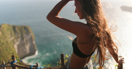 Young woman enjoying the ocean view on nusa penida island in bali, her hair blowing in the windの写真素材