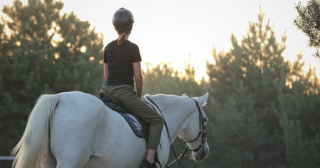 Young woman riding a white horse in a forest, enjoying the beautiful sunset during a horseback riding tour, promoting equestrian tourism and a connection with natureの写真素材