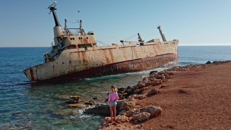 Woman standing on the rocky seashore admiring the iconic rust-covered Edro III Shipwreck grounded on...