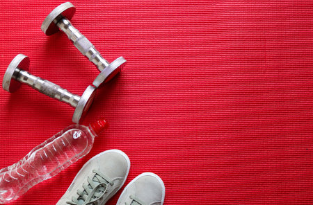 sport equipments, dumbbells, bottle with water and sneakers on the red background. Flat lay, top view. Healthy lifestyle, sport and weight loss conceptの写真素材