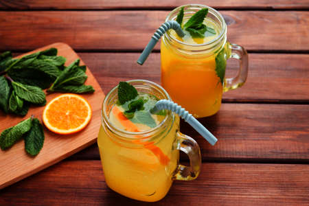 Summer refreshment drinks. Lemonade in jars with ice, mint and oranges on a wooden table close-up.