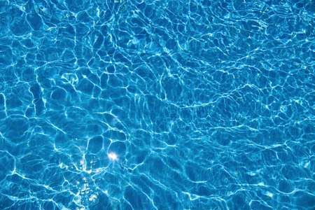 Abstract summer background with clear blue water in the swimming pool and sun reflection. Ripple...