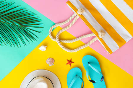 Summer flat lay. Palm leaf, beach bag, summer hat, flip-flops and seashels on a yellow, pink and turquoise background. Vacation and fashion concept. Top viewの写真素材