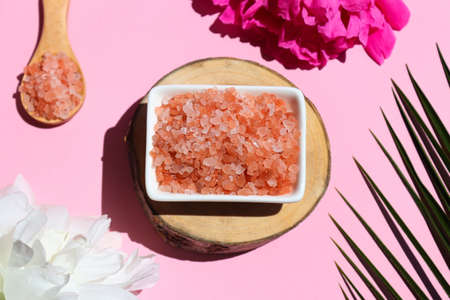 Beauty and spa concept. Pink himalayan salt on a wooden cut with palm leaf and peony flowers....