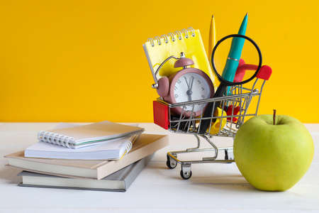Back to school concept. Grocery cart with school supplies, green apple, note pads and books on the...