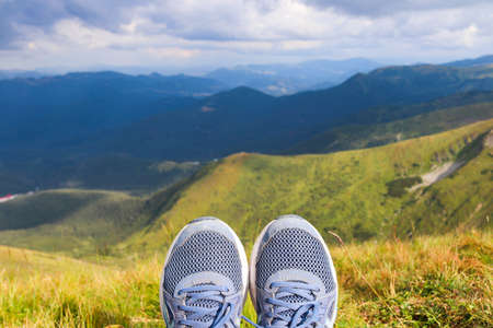 Blue sneakers of the traveler against the background of mountain landscapes. Tourism and travel concept. Selective focusの写真素材