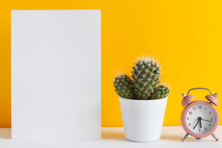Mockup with paper blank, alarm clock, and cactus, or succulent against yellow wall with copy space for text. Place for text. Minimalismの写真素材