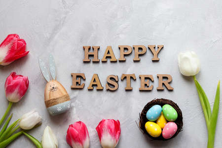 Festive composition with tulips, Easter bunny, decorative colored eggs in nest, and the inscription...
