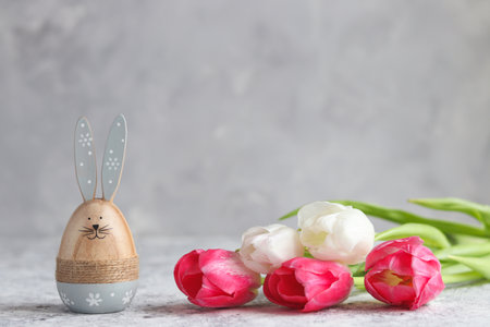Festive Easter composition with tulips and Easter bunny against grey wall. Holiday greeting card....
