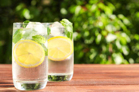 Fresh homemade citrus lemonade with lemons, mint and ice on a wooden table against greenery. Summer cold refreshing drinks. Selective focus, copy spaceの写真素材