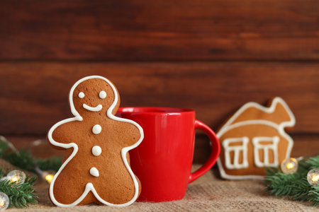 Christmas festive composition. Gingerbread man cookie and house coockie, red cup with tea or coffee, Christmas tree branches with lights against wooden background. Selective focusの写真素材