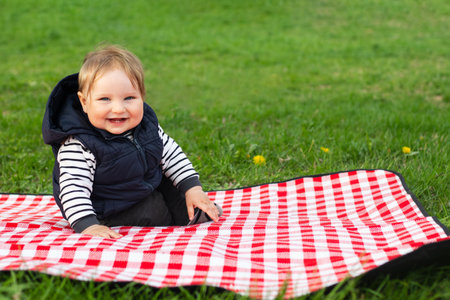 Happy laughing child sitting on blanket outdoor. Springtime. Copy space for text