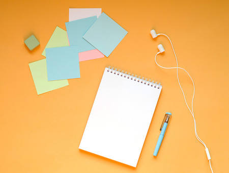 Stationery and headphones lie on a juicy orange background.