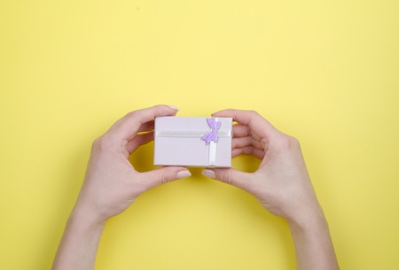 A small purple gift box with a bow in his hands on a lilac background.