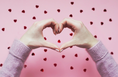 Hands folded heart on pink background with red hearts. Love