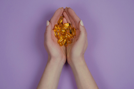 Yellow fish oil in tablets on purple background. Vitamins