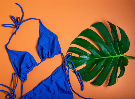 Beach concept. Blue swimsuit and leaf monstera on warm orange background.の写真素材