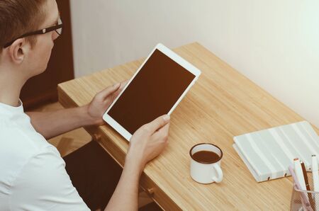 A young man sitting at his Desk, reading on a tablet.の写真素材