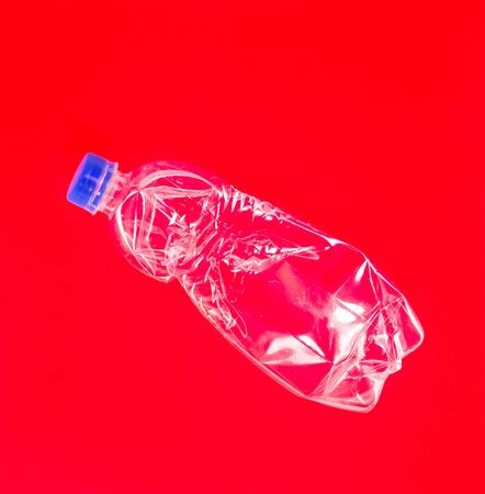 Crumpled clear plastic bottle on a red background. Spectacular photoの写真素材