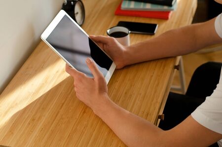A young man sitting at his Desk, reading on a tablet.