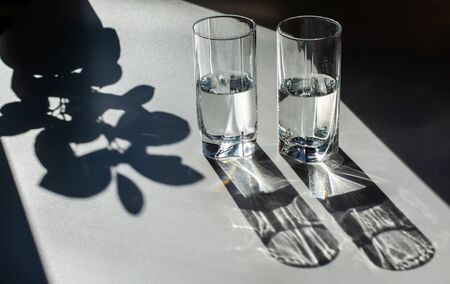 Two glasses of water. Bright light and contrasting shadows. Sun glare.の写真素材