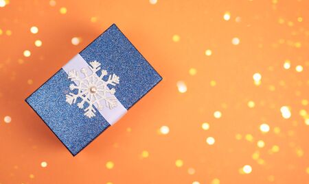 Blue shiny Christmas gift with snowflake on orange background. A festive composition. Christmas photo.の写真素材