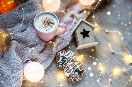 Cup of coffee with cinnamon. Christmas background with lights, warm knitted scarf. The atmosphere of...