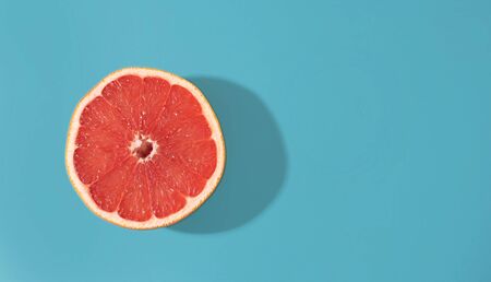 Bright red-orange grapefruit in a section on a blue background. Bright contrast photo.の写真素材