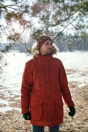 A young man in a red jacket on the background of the lake. Pine forest.